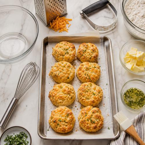 Baking equipment for homemade cheddar biscuits including baking sheet, grater, and pastry cutter
