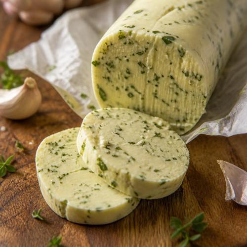 Chilled log of garlic herb butter partially unwrapped with two sliced medallions