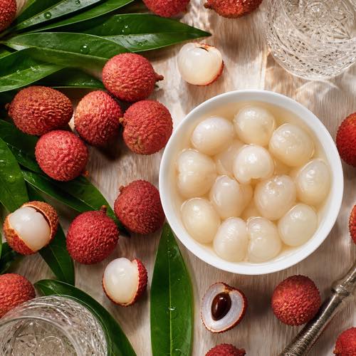 Fresh bumpy red lychee fruits, peeled translucent lychees, and canned lychees in syrup